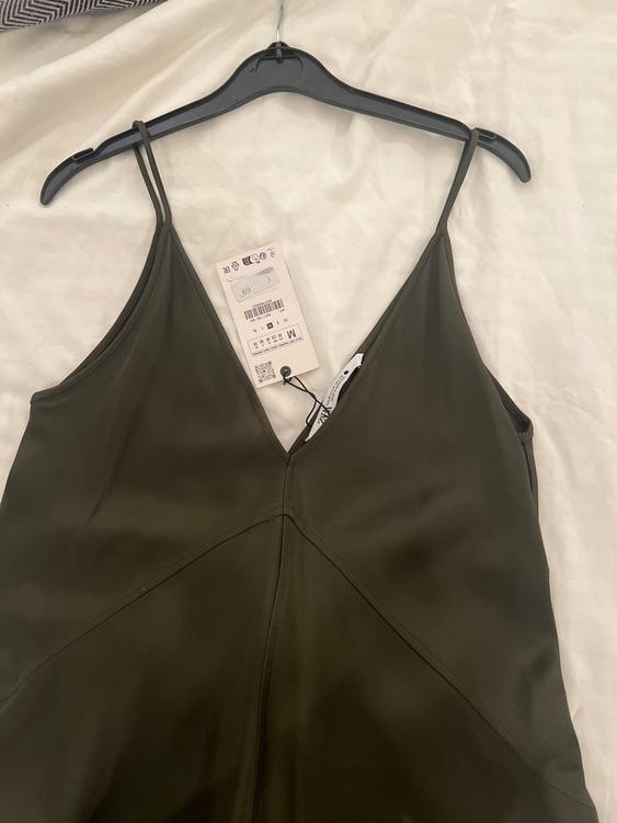 Olive green dress with thin straps on a black hanger over a white bed. Visible tag with barcode and size M.