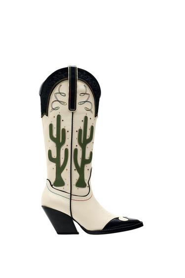 Side view of a white cowboy boot with a green cactus design and black detailing.