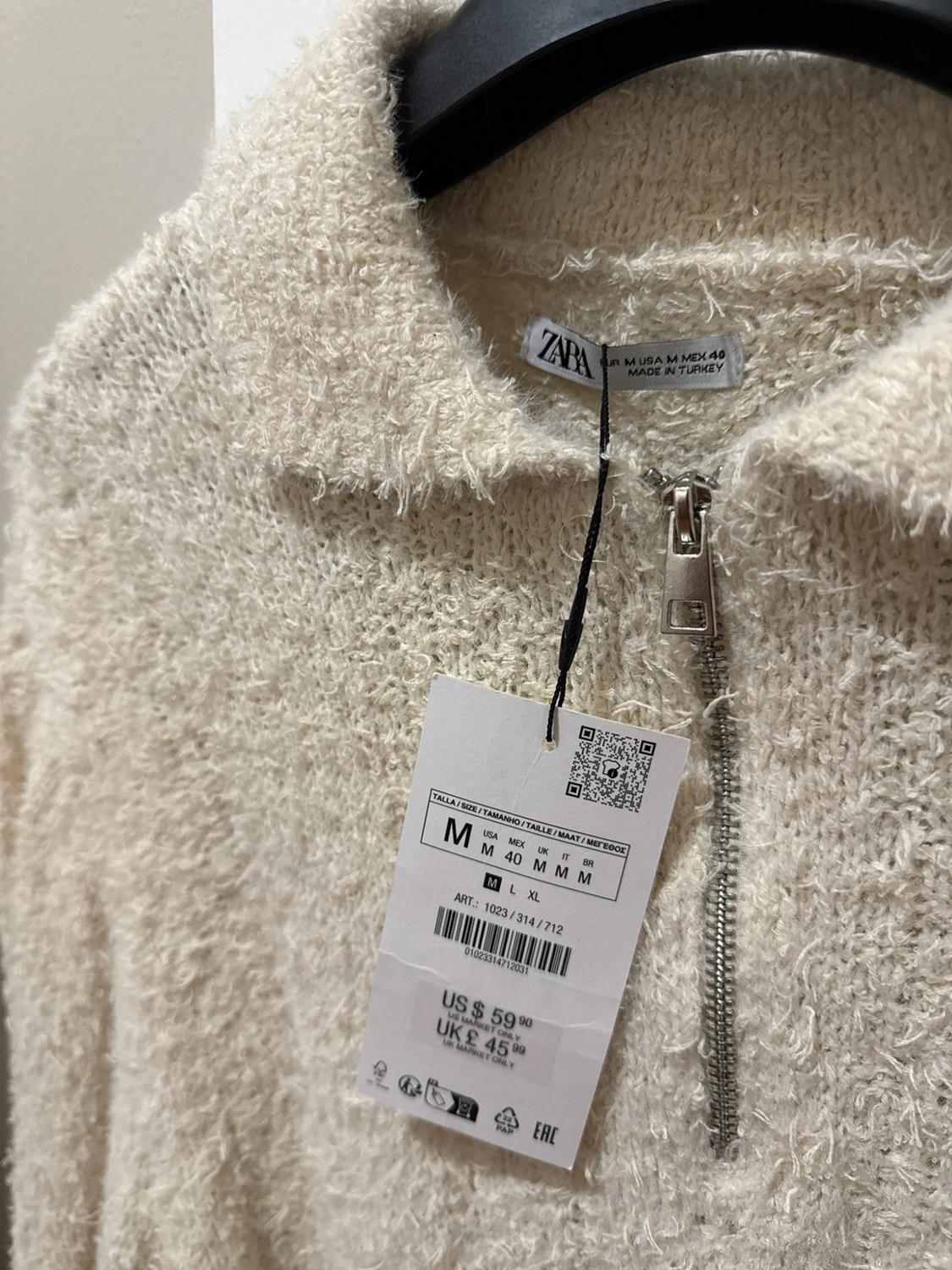 Textured ecru sweater with zipper and tags. Text: ZARA, EUR M USA M MEX 40, ART.: 1023/314/712, US $59.90, UK £45.99.