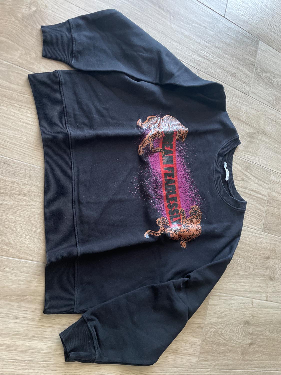 Black sweatshirt with tiger print and "TEAM FIERCE" text in red and pink. Light wood background.