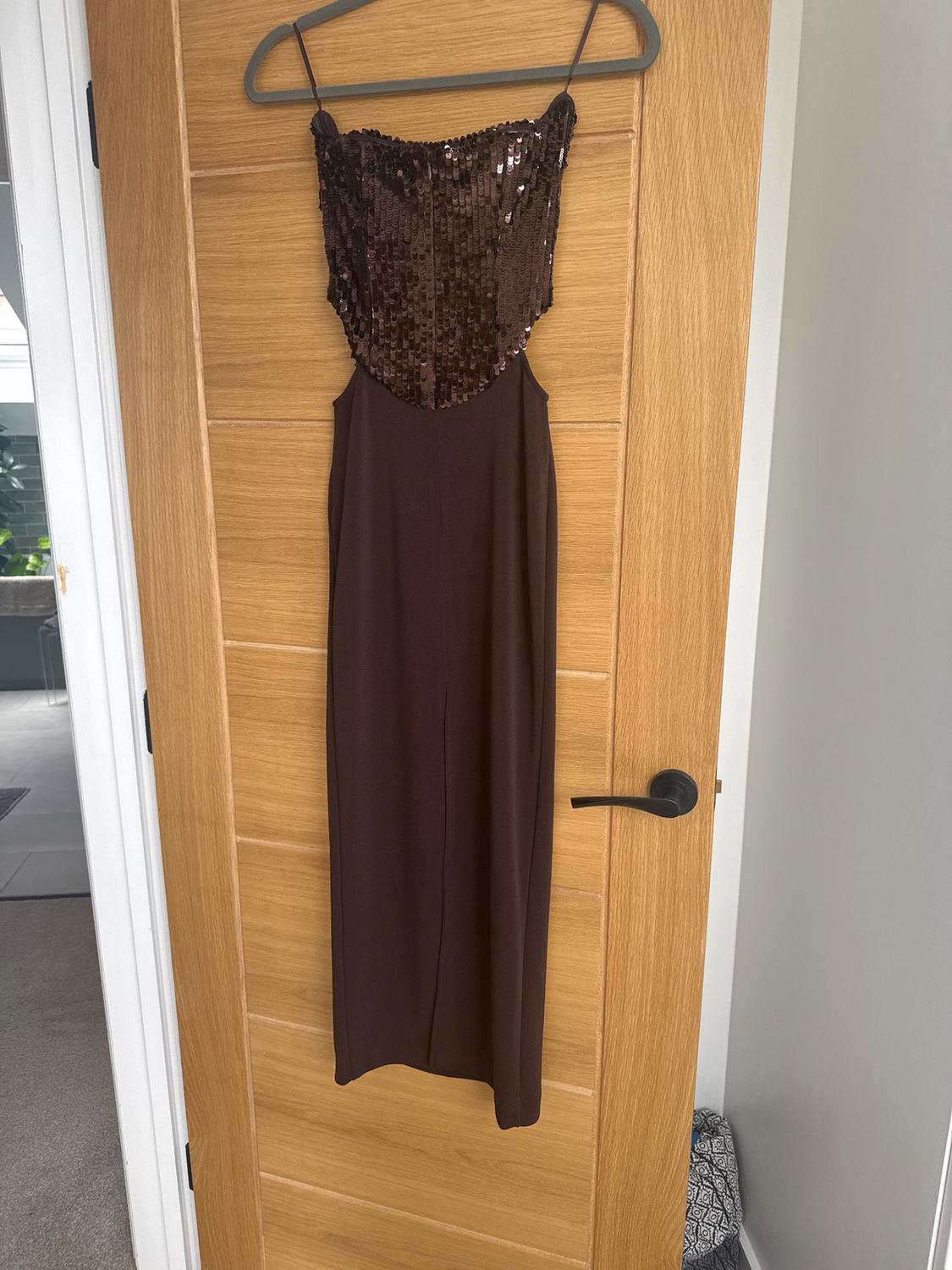 Brown sequined dress hanging on a light wood door. Modern indoor setting.