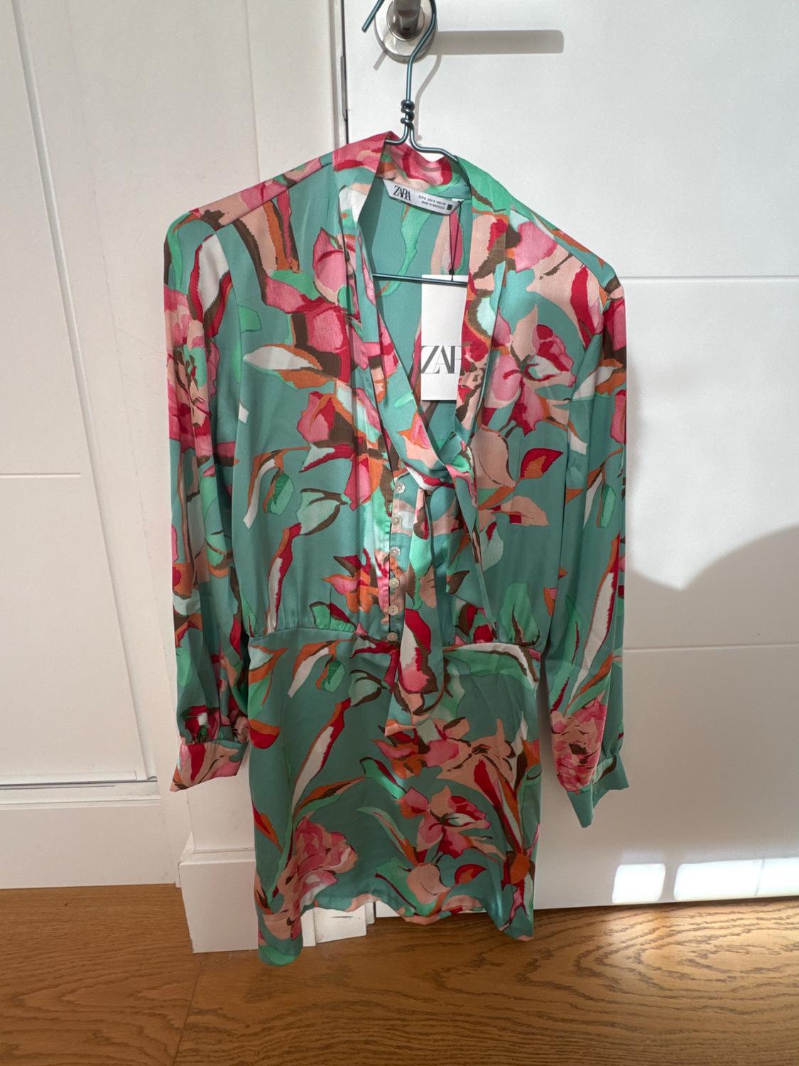 Dress hanging on a hanger, with a floral pattern in shades of green, pink, and red. Visible label with the text "ZVN".