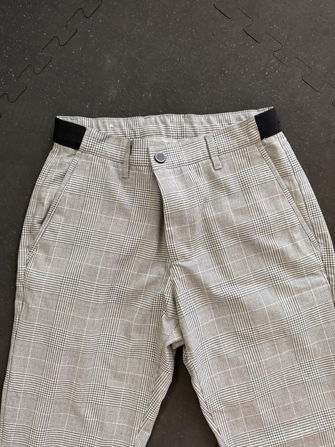Gray plaid pants with a black elastic waistband, on a black rubber background with a puzzle texture.