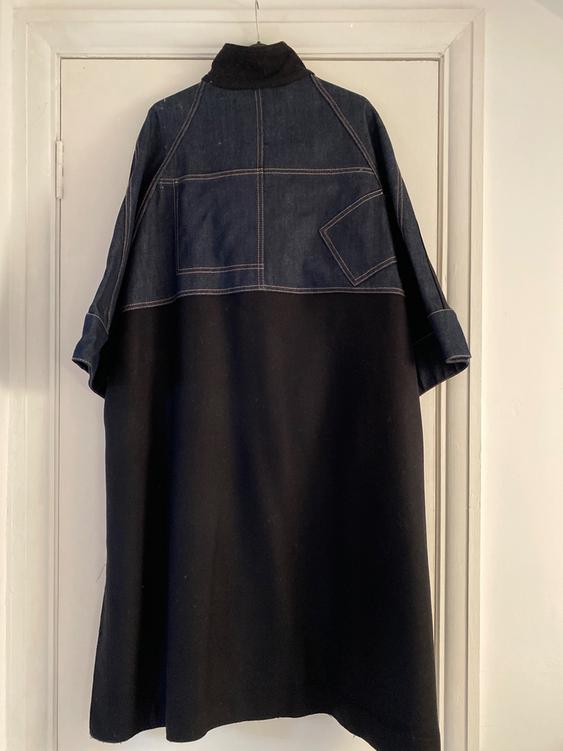 Coat hung on a door, with blue denim top and black bottom, visible seams in the design.