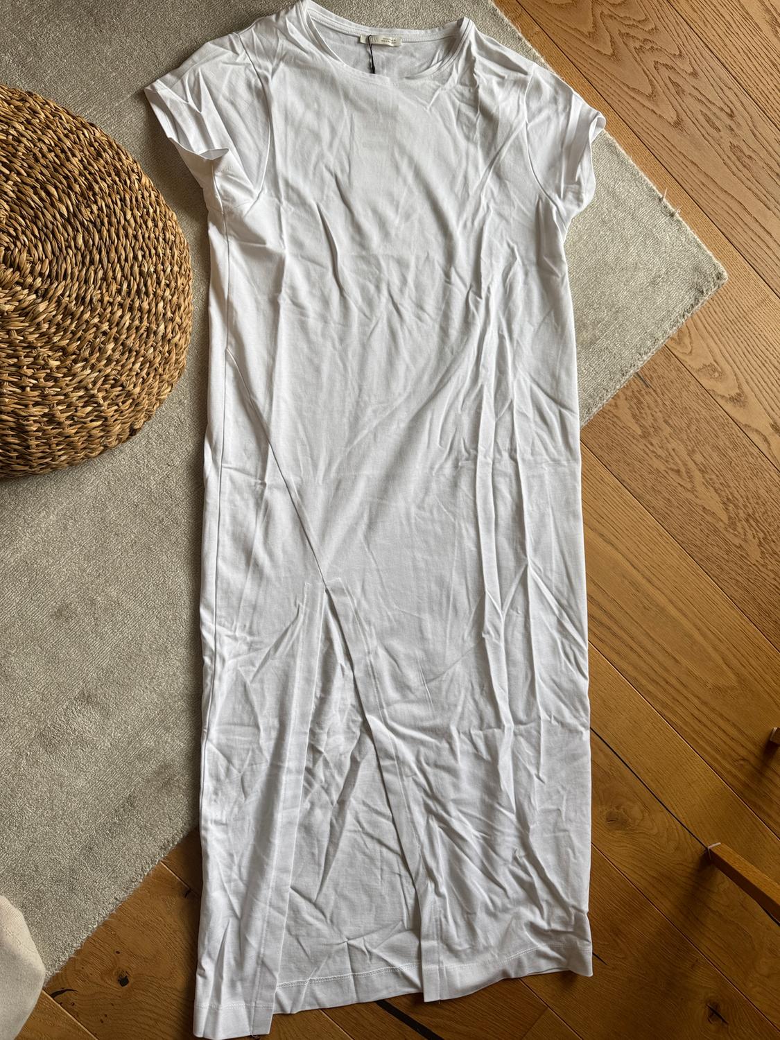 Creased white short-sleeved dress on a beige rug and wooden floor. To the left, a wicker basket.