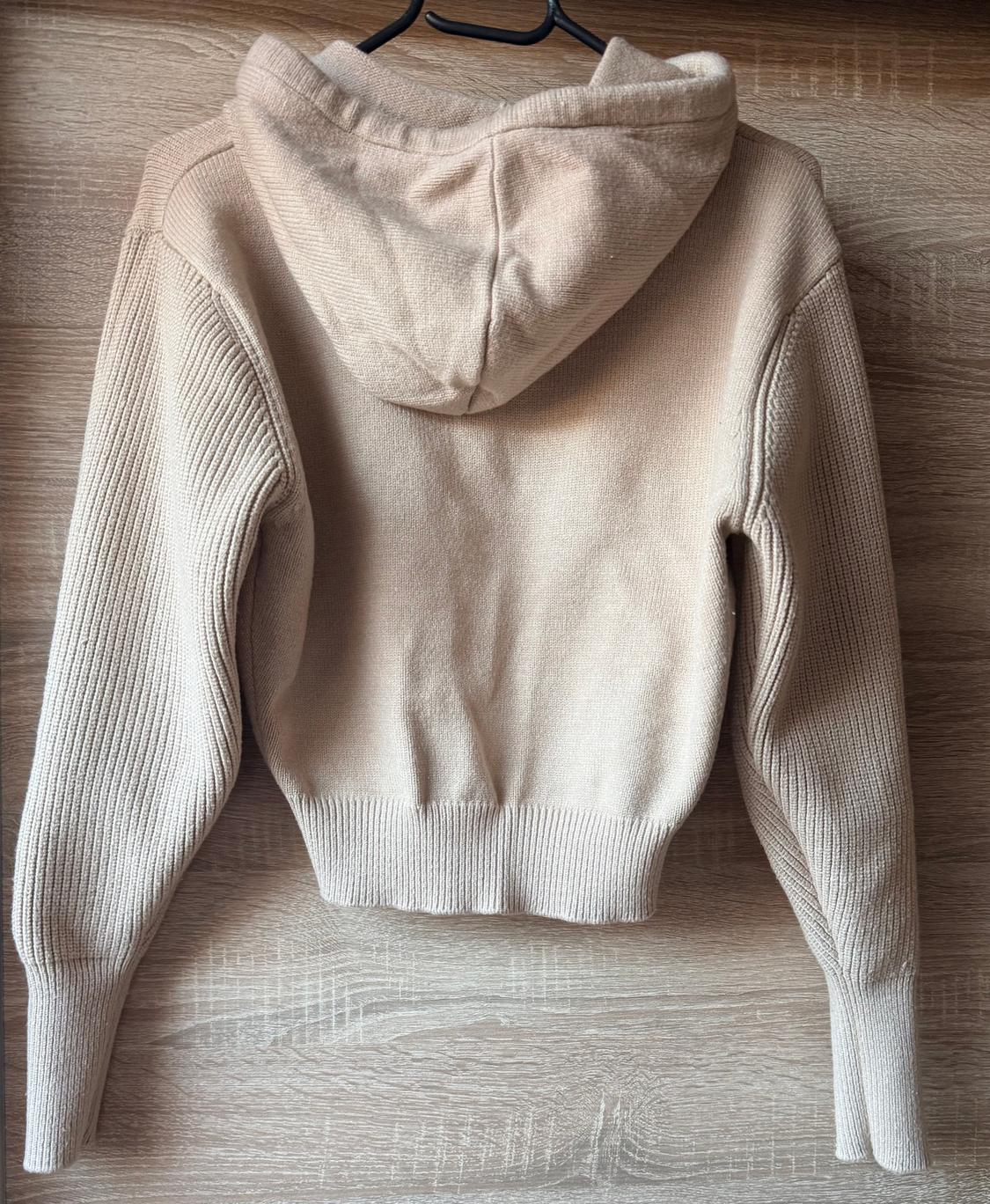 Beige hoodie hanging on a hanger against a light wood background. Ribbed knit sleeves and body.