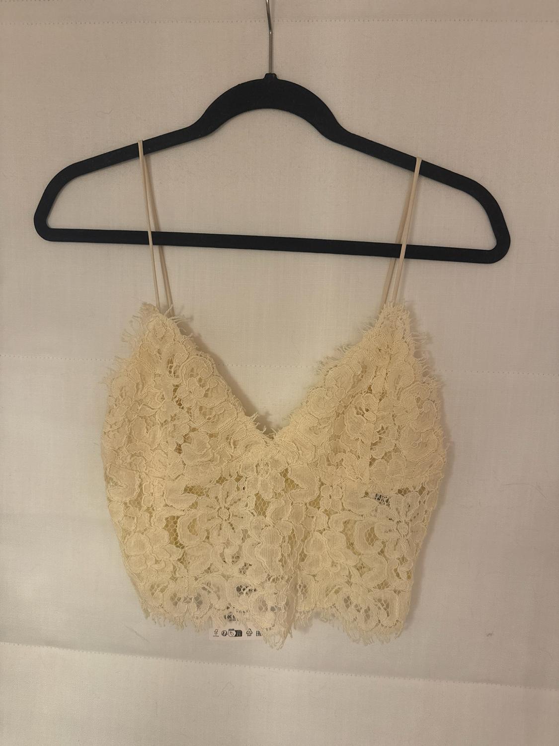 Cream floral lace crop top with thin straps and a V-neckline, hanging from a black hanger against a plain white background.