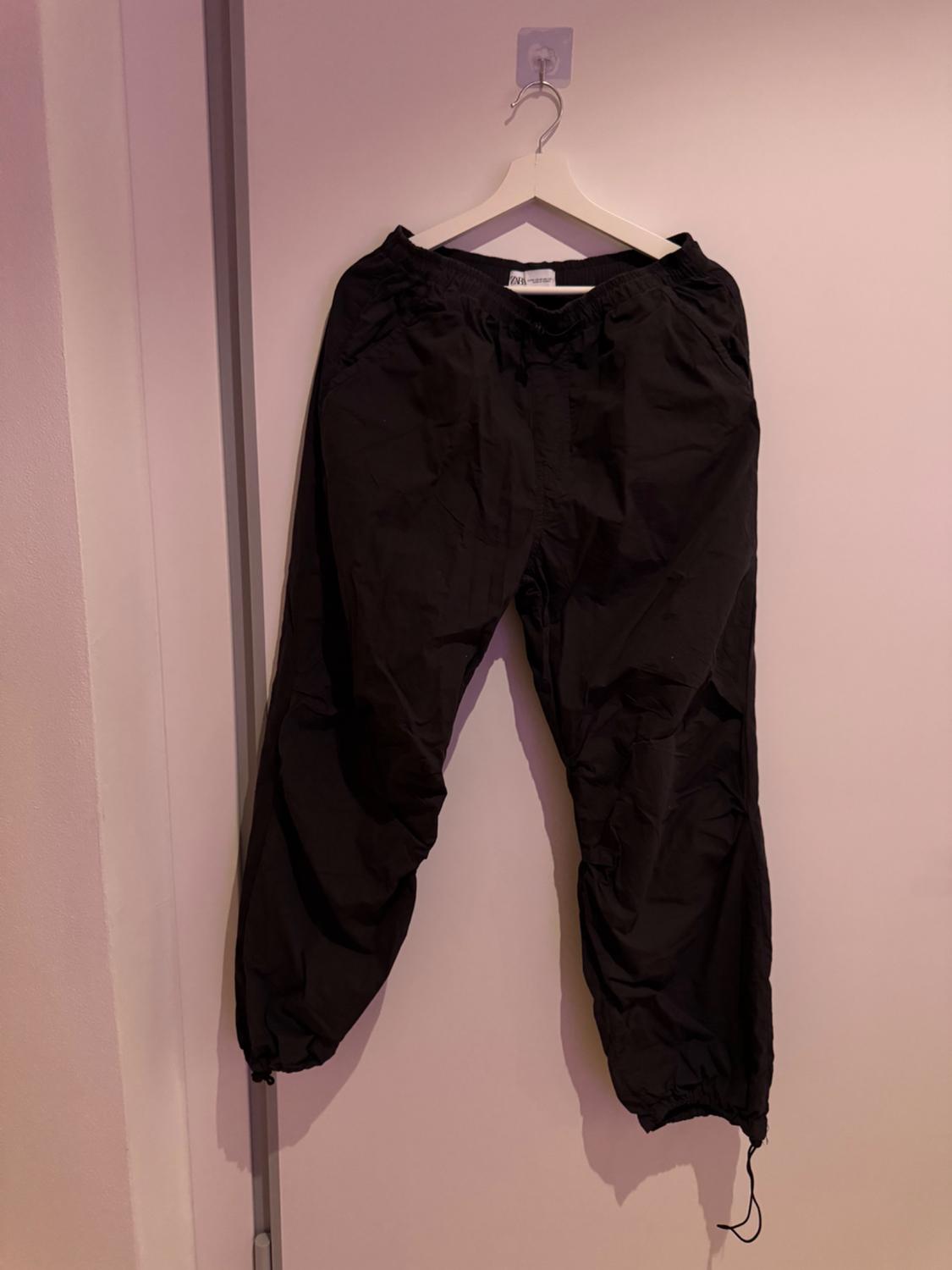 Front view of black trousers with elasticated waist and cuffed ankles.