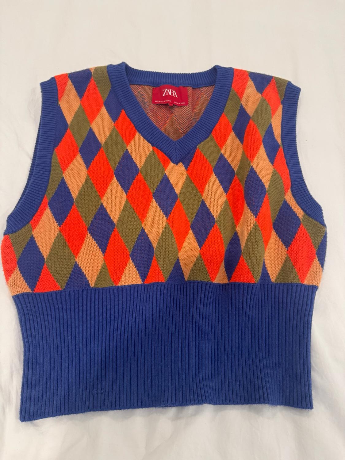 Knitted waistcoat with a V-neck, multicoloured diamond pattern and blue ribbed hem on a white background. Inner label with ZARA text.