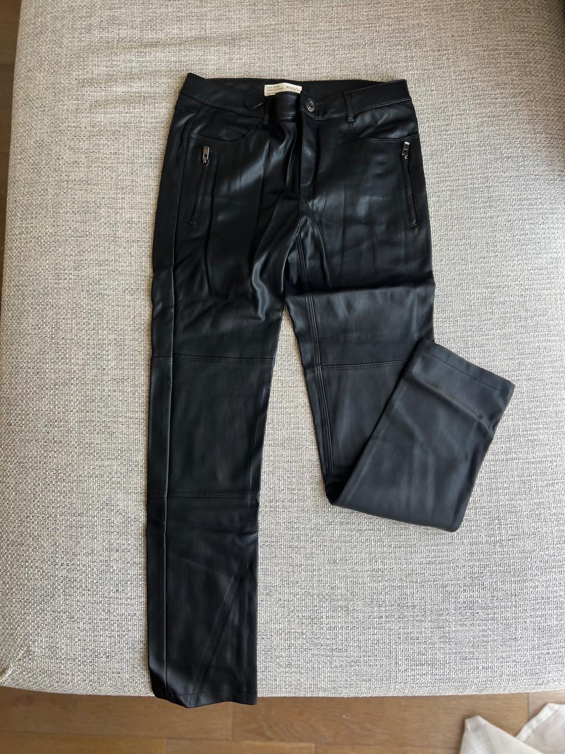 Black synthetic trousers with zipped pockets, placed on a light grey sofa.