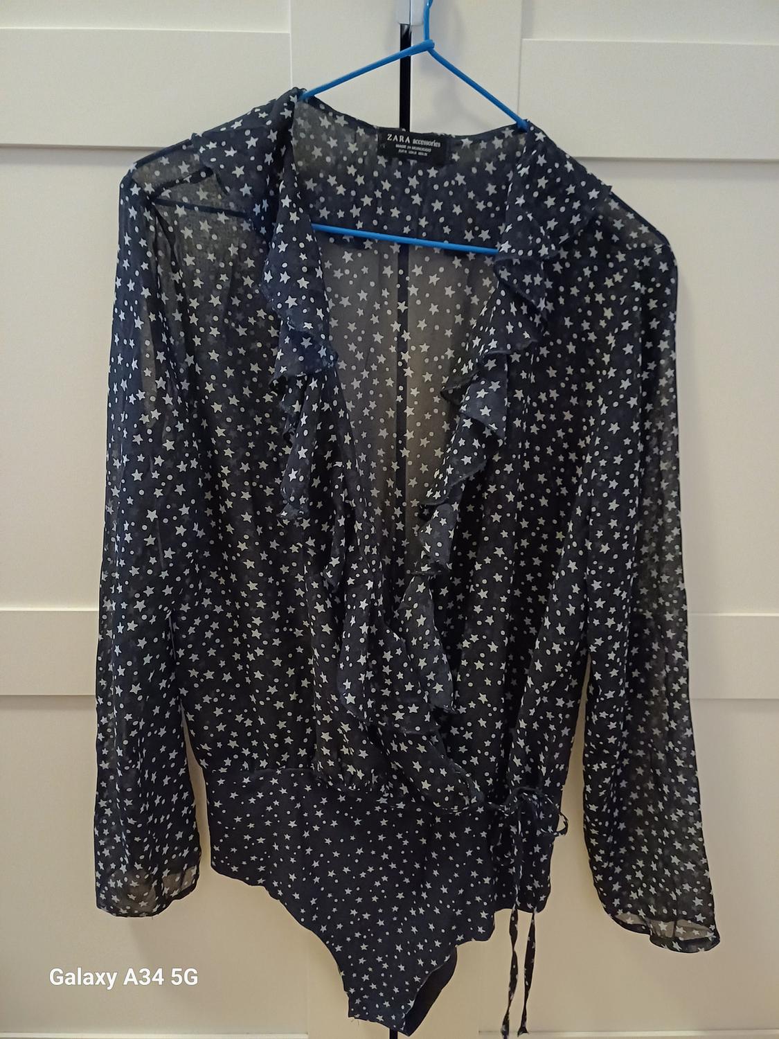 Front view of a sheer black blouse with a star print and ruffles on the neck and long sleeves.