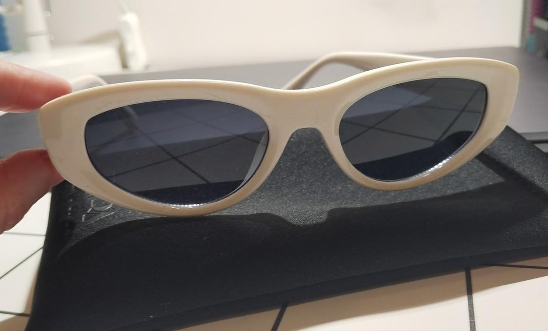 White-framed sunglasses with dark lenses on a black case. Hand holding them indoors.