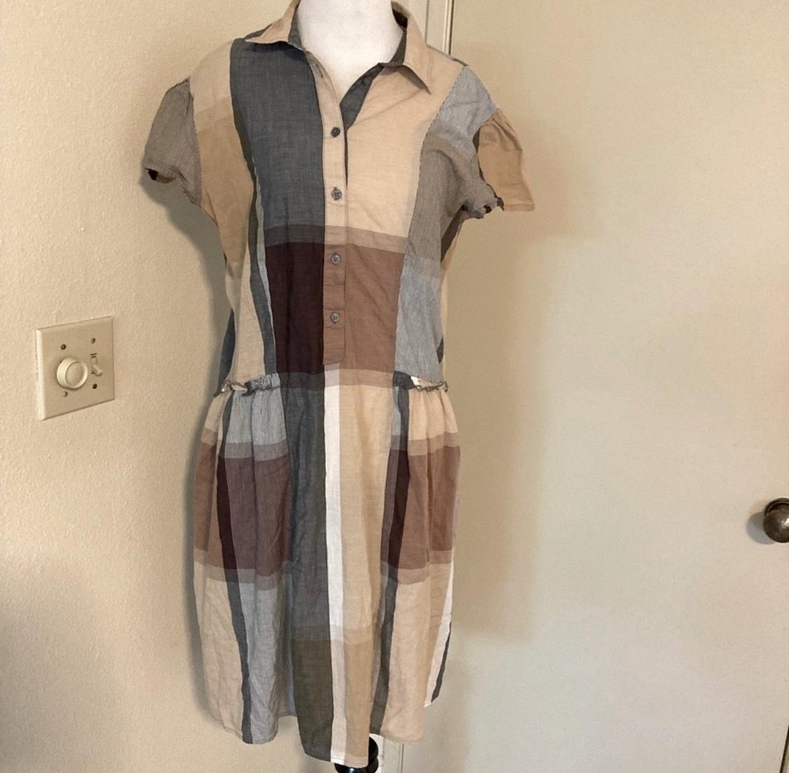 Checked dress in shades of brown and beige on a white mannequin, with front buttons and short sleeves, in a room.