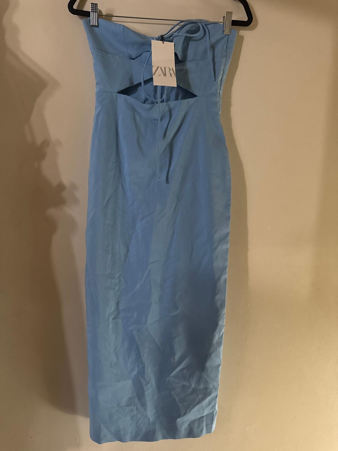 Light blue strapless dress hanging on a hanger, with a visible "ZARA" tag. Beige background with soft shadows.