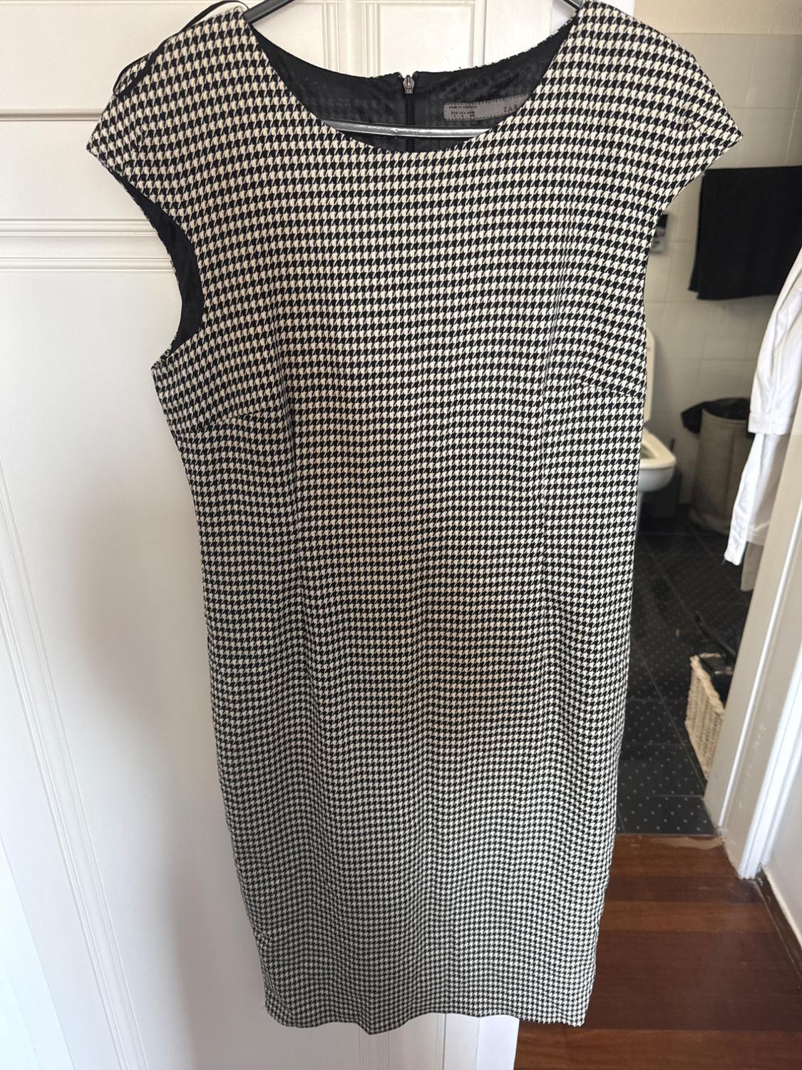 Sleeveless black and white houndstooth dress, hanging on a hanger over a white door.
