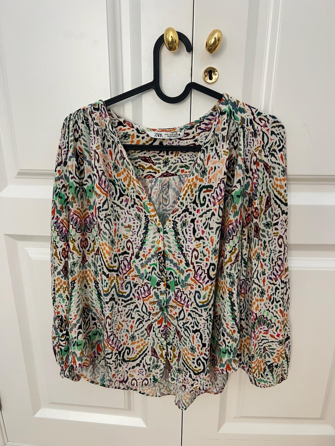 ZARA blouse with a colourful abstract print, V-neck and long sleeves, hanging on a black hanger over a white door.
