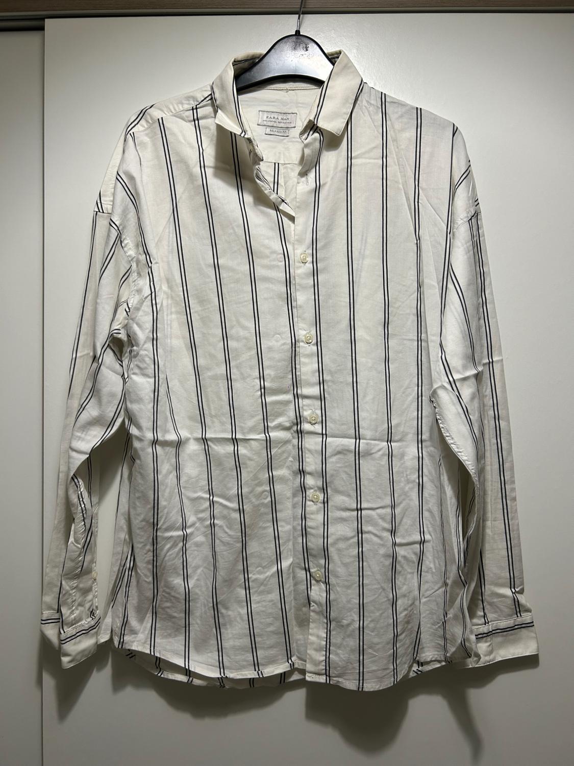 White long-sleeved shirt with black vertical stripes, hanging on a black hanger against a white background.