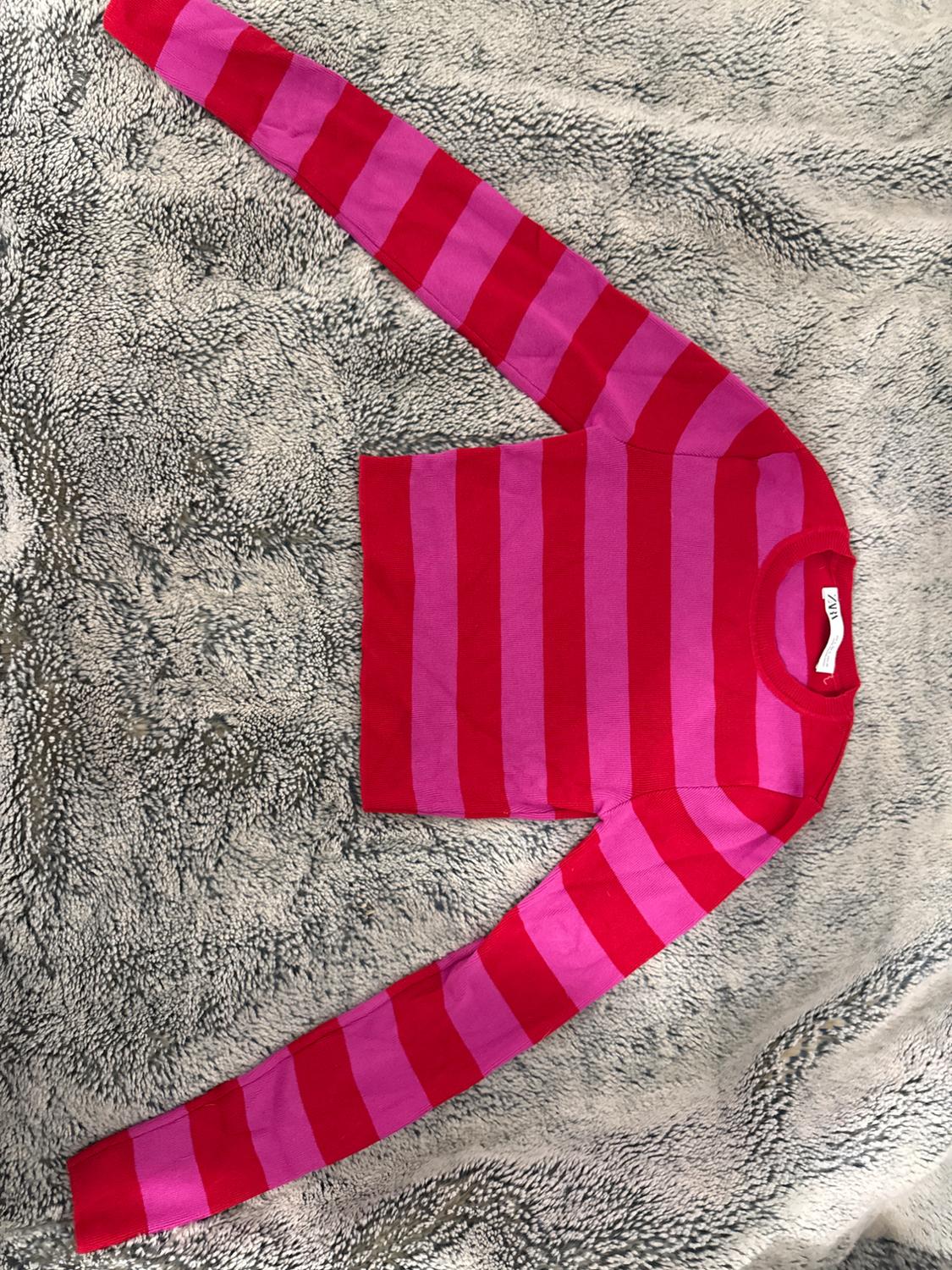 Red and pink horizontal striped jumper on a fluffy textured blanket in shades of grey. Visible label on the collar.