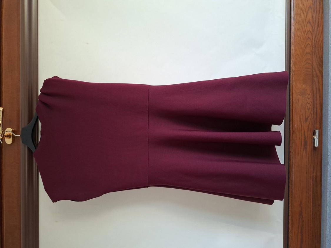 Burgundy sleeveless dress hanging on a black hanger, with a flared skirt, on a white background and wooden frame.