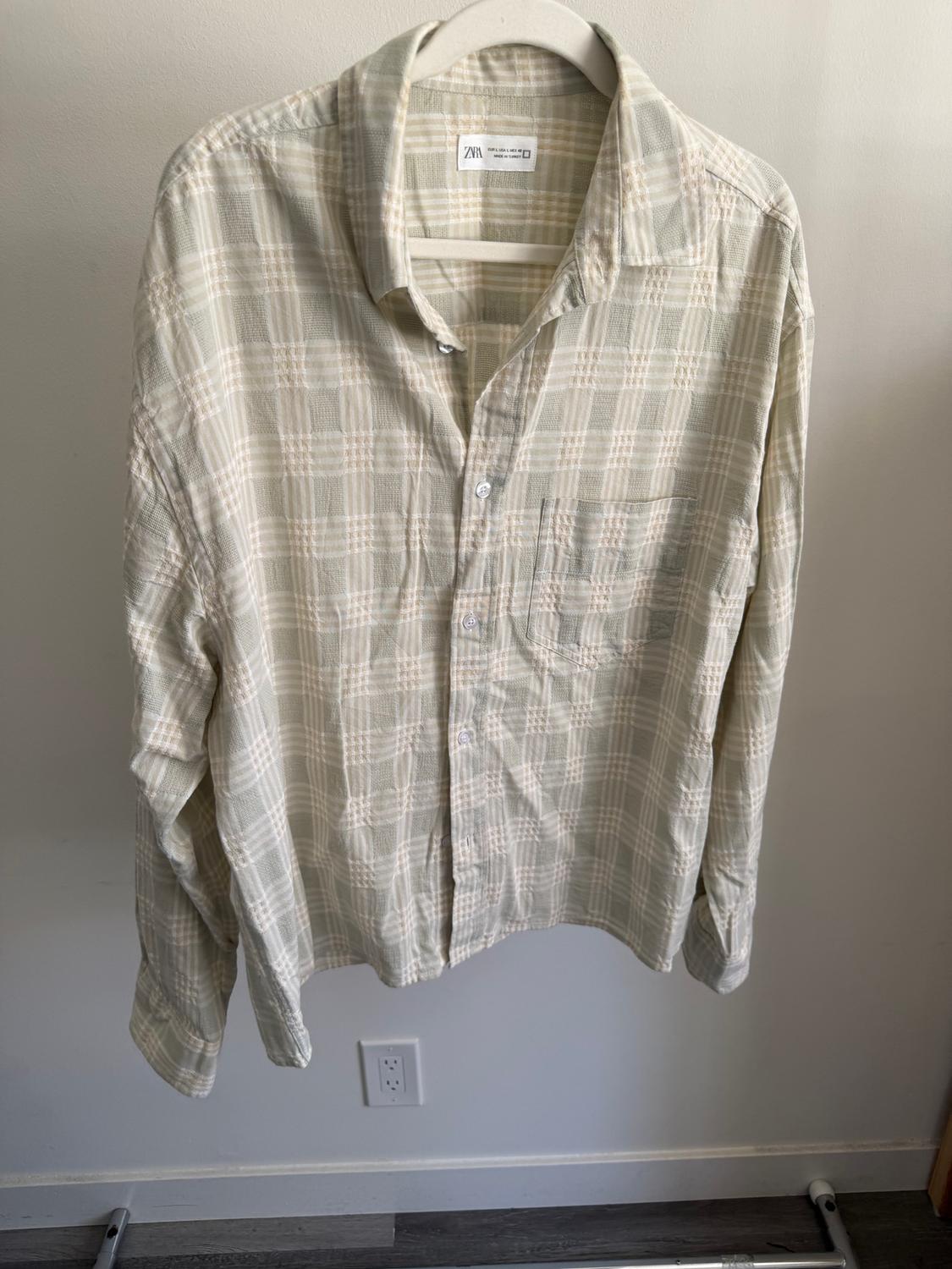 Light-coloured checked shirt hanging on a white hanger. Visible label on the collar with a brand logo.