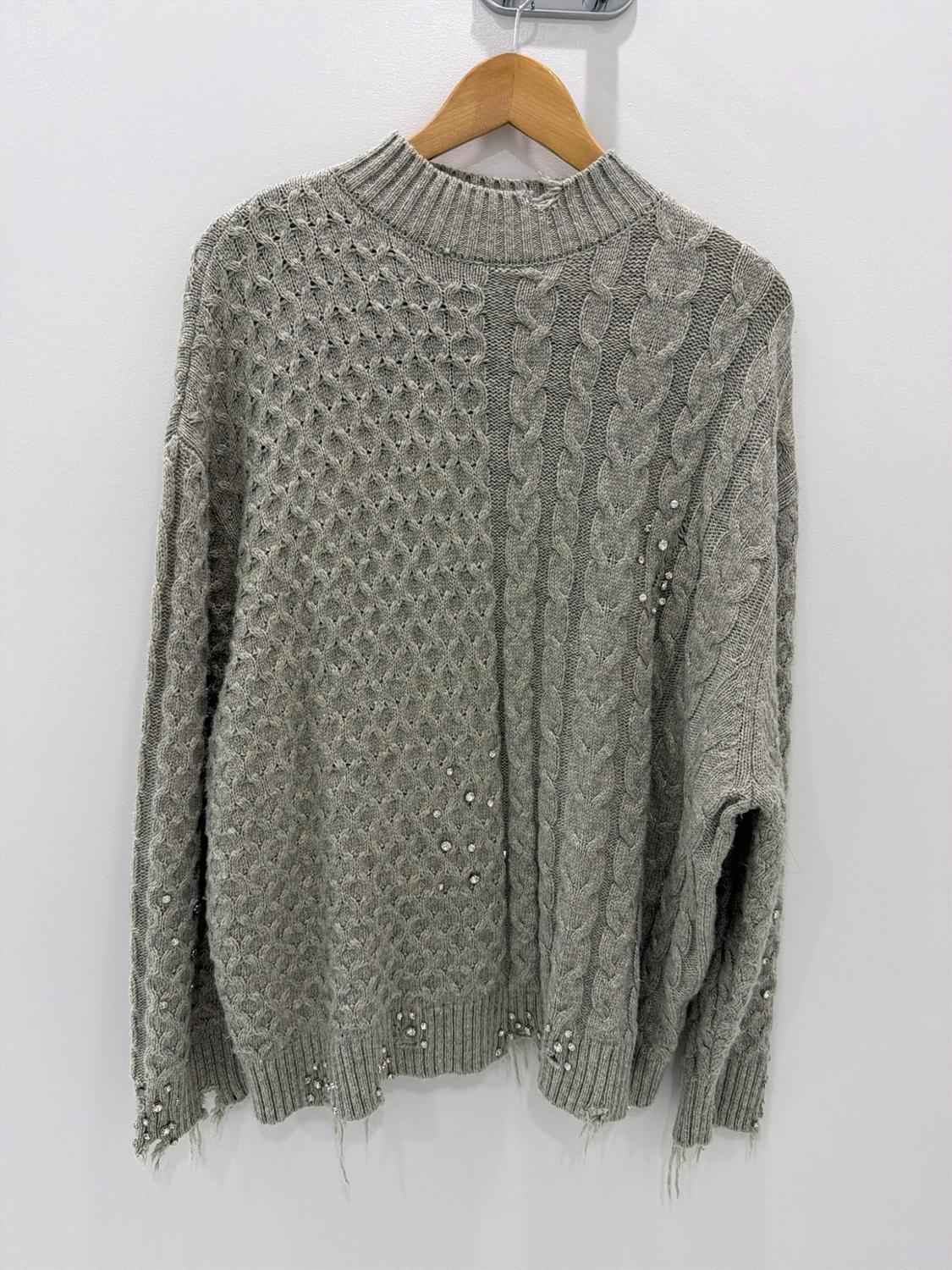 Gray knit sweater with a mix of textures, shiny details, and a frayed hem, hanging on a wooden hanger against a white wall.