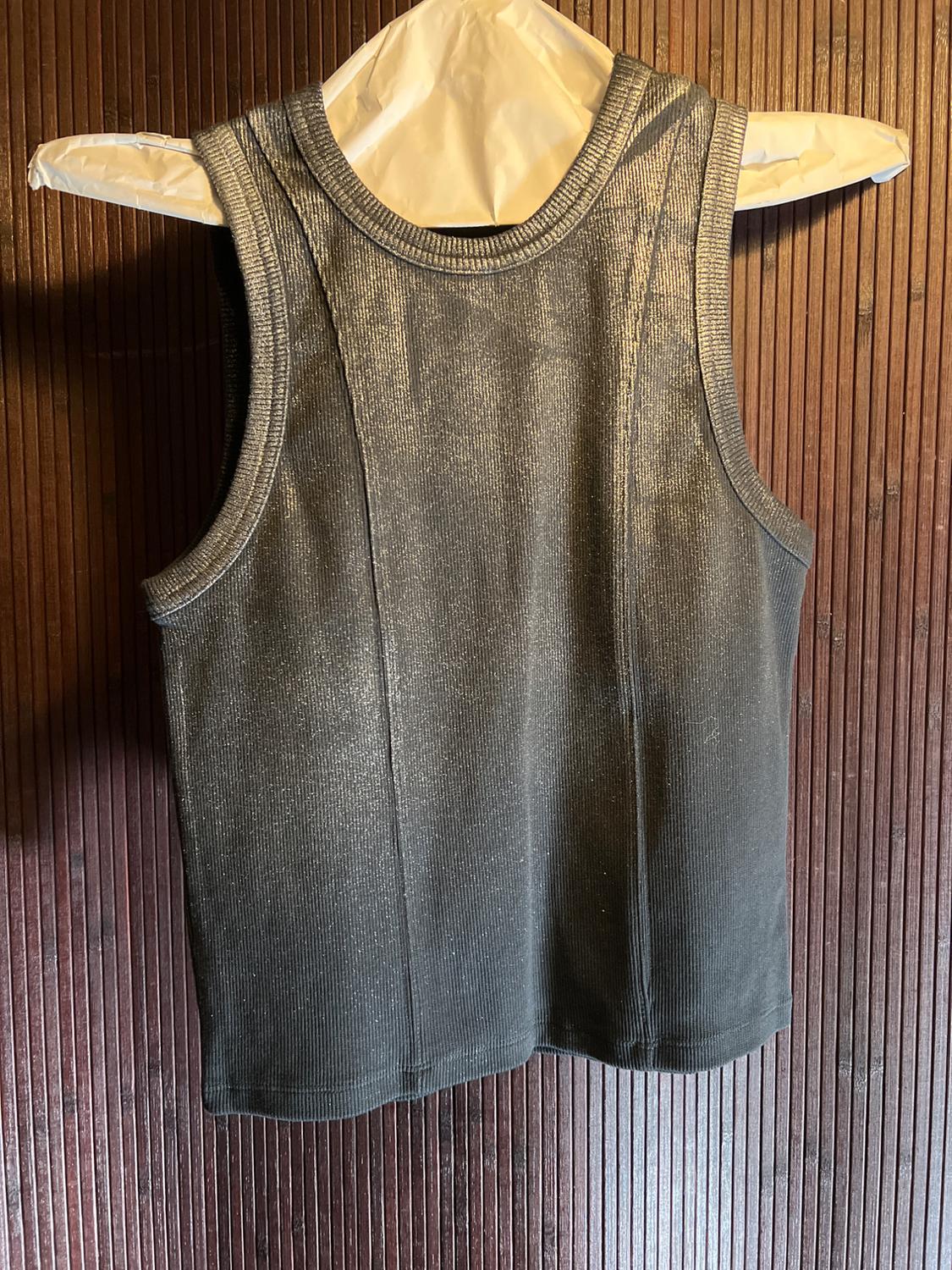 Gray glitter tank top hanging on a white hanger, against a brown wooden background with vertical texture.