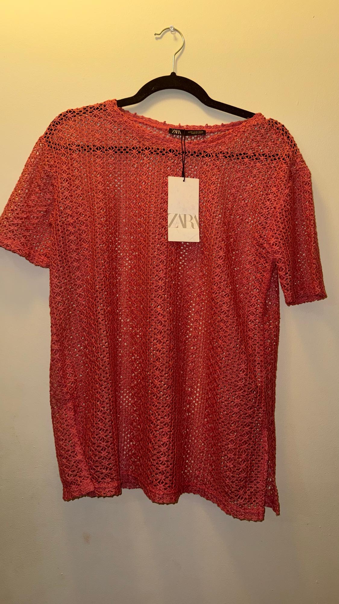 Red crochet blouse hanging on a black hanger with a Zara tag. Plain white background.