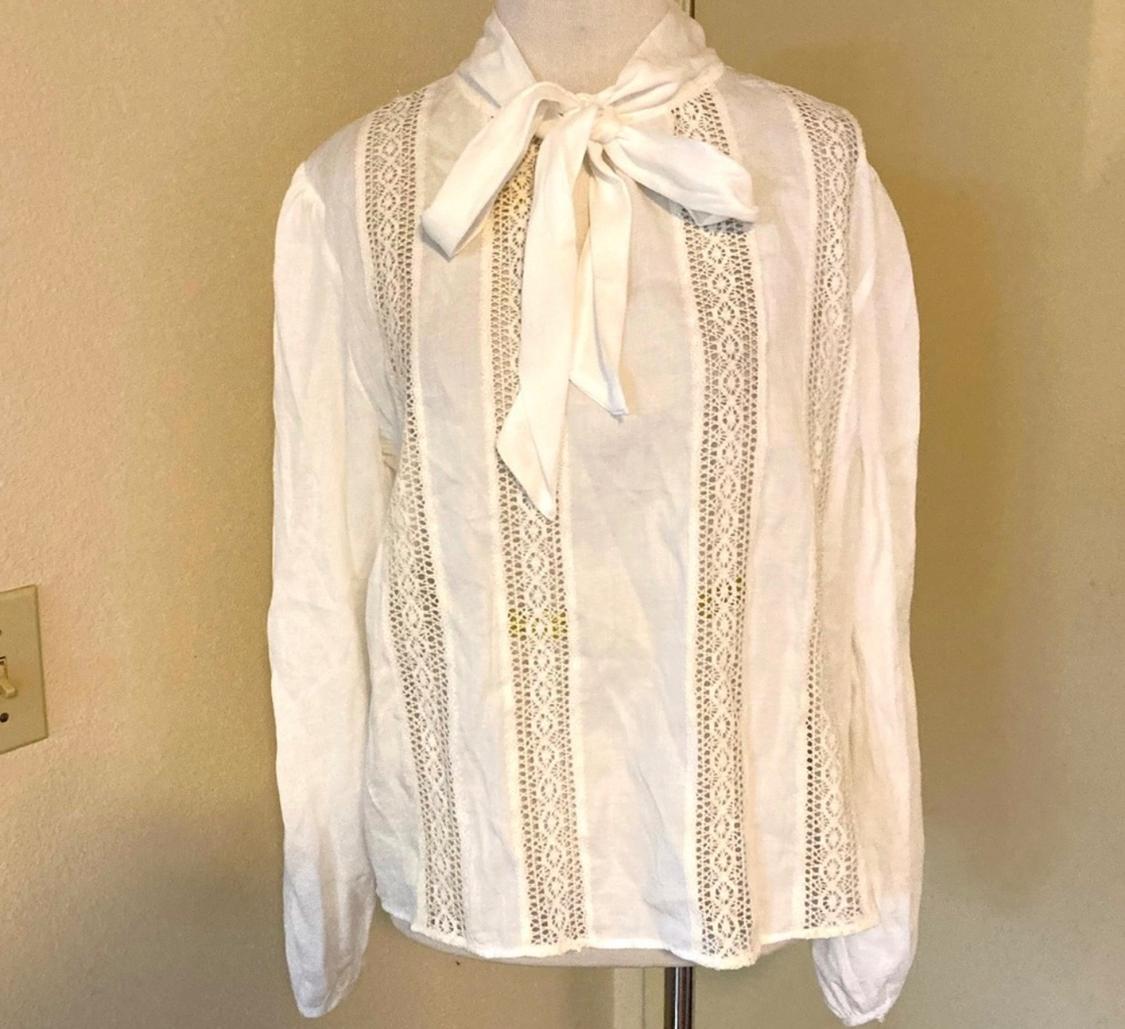 White lace blouse with a bow at the neck, displayed on a mannequin against a beige background.