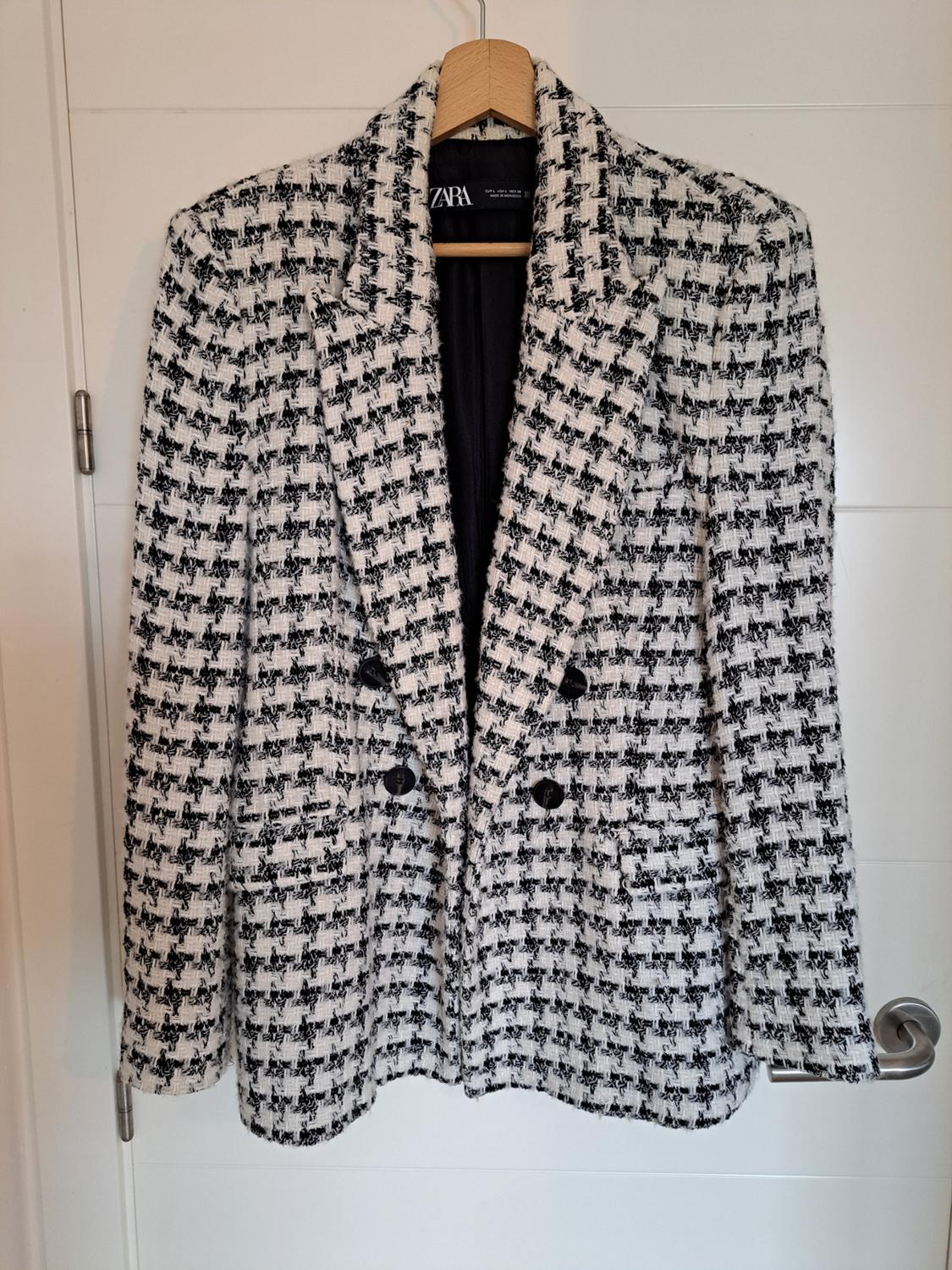 Black and white checked jacket hanging on a wooden hanger. Visible ZARA brand label inside.