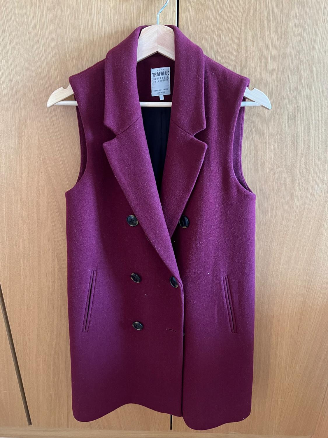 Burgundy long waistcoat with lapel collar and double-breasted buttons on a wooden hanger. Text: ZARA TRAFALUC OUTERWEAR COLLECTION.