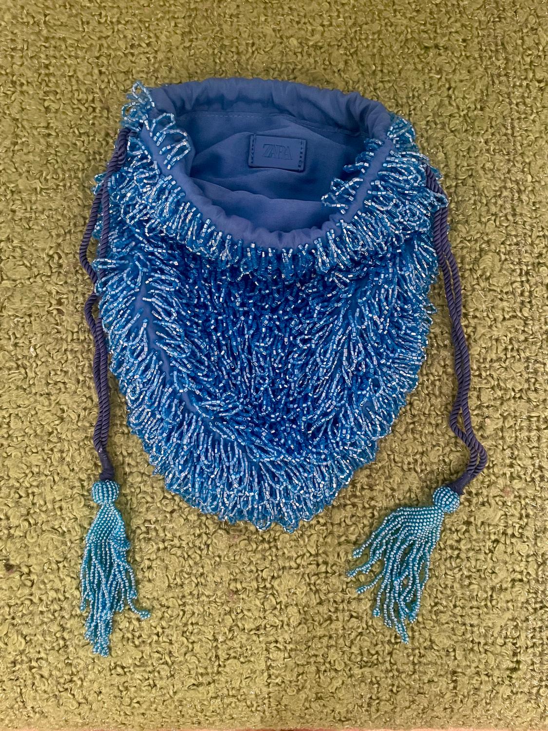 Blue bag with shiny beads and tassels, on a green rug. Internal label with text "ZARA".