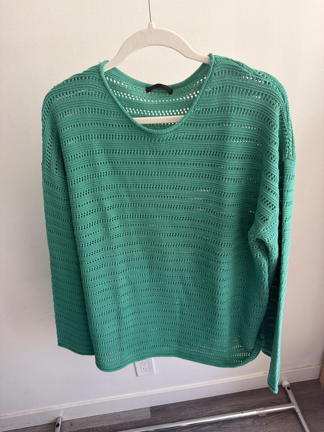 Green open-knit jumper hanging on a white hanger against a light background.