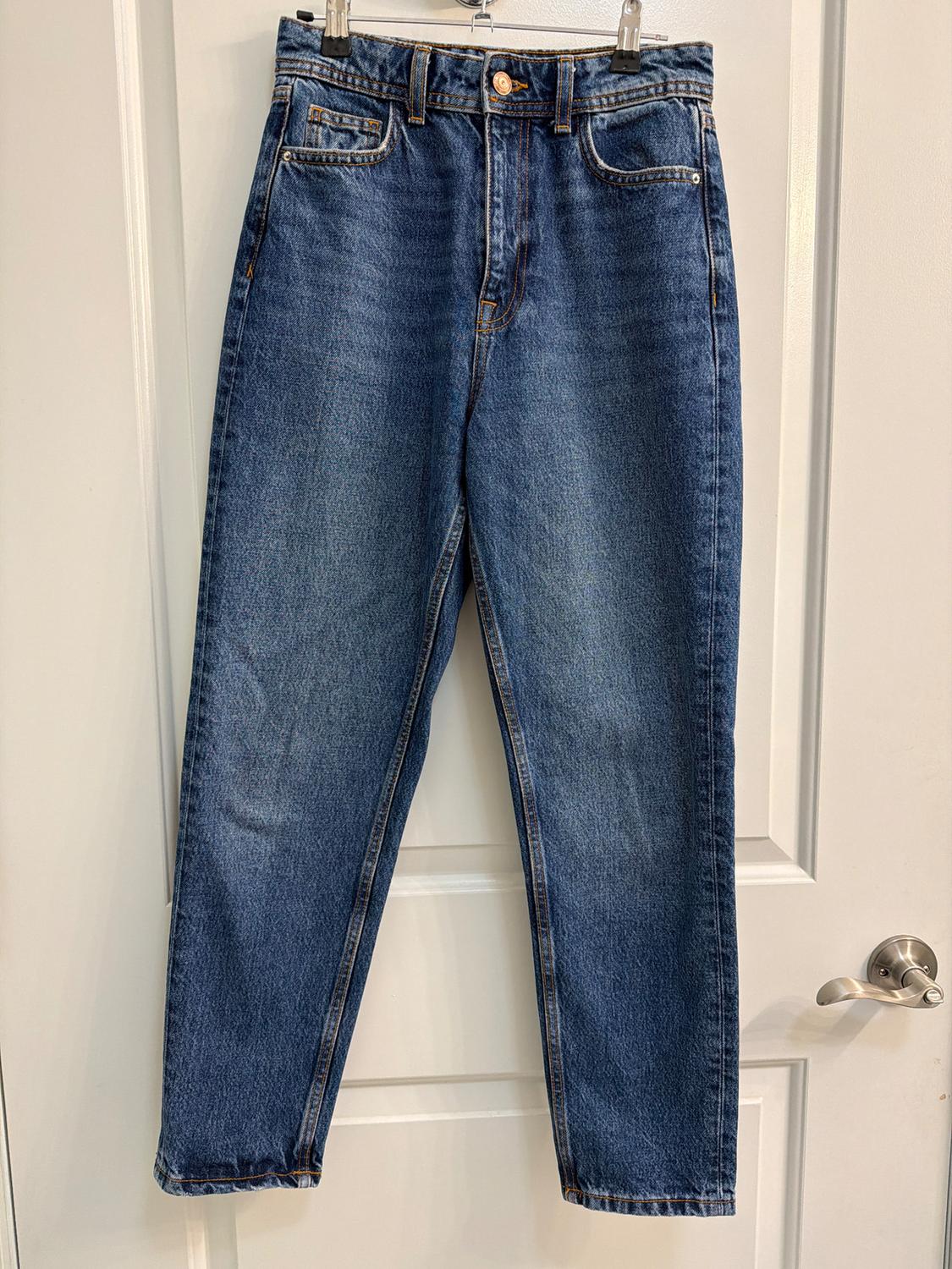 Blue jeans hanging on a white door, with visible stitching and a metal button at the waist.