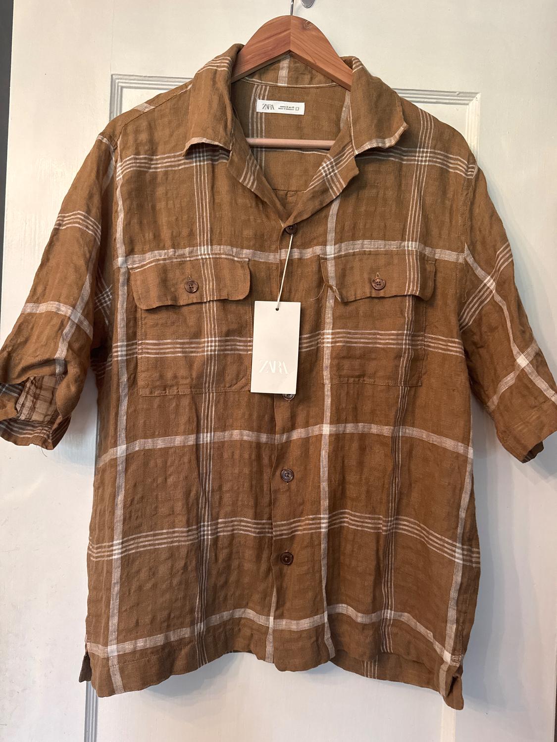 Brown and white checked shirt hanging on a wooden hanger. Visible label with the text "ZARA".