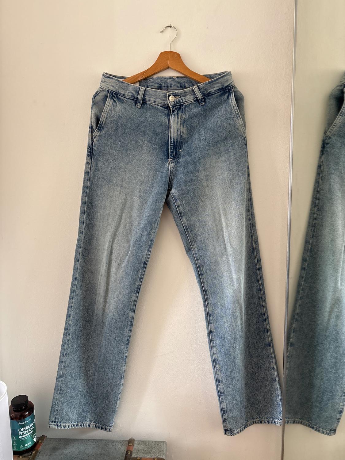 Light blue jeans hanging on a wooden hanger against a white wall. Below is a trunk and a jar with the text OMEGA FISH OIL.