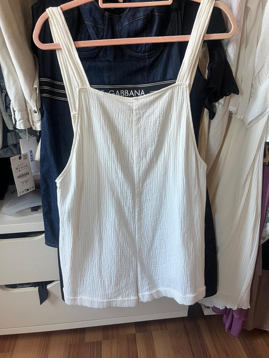 White strappy top hanging on a pink hanger, against a background of various clothes in a wardrobe. Visible text: "GABBANA".