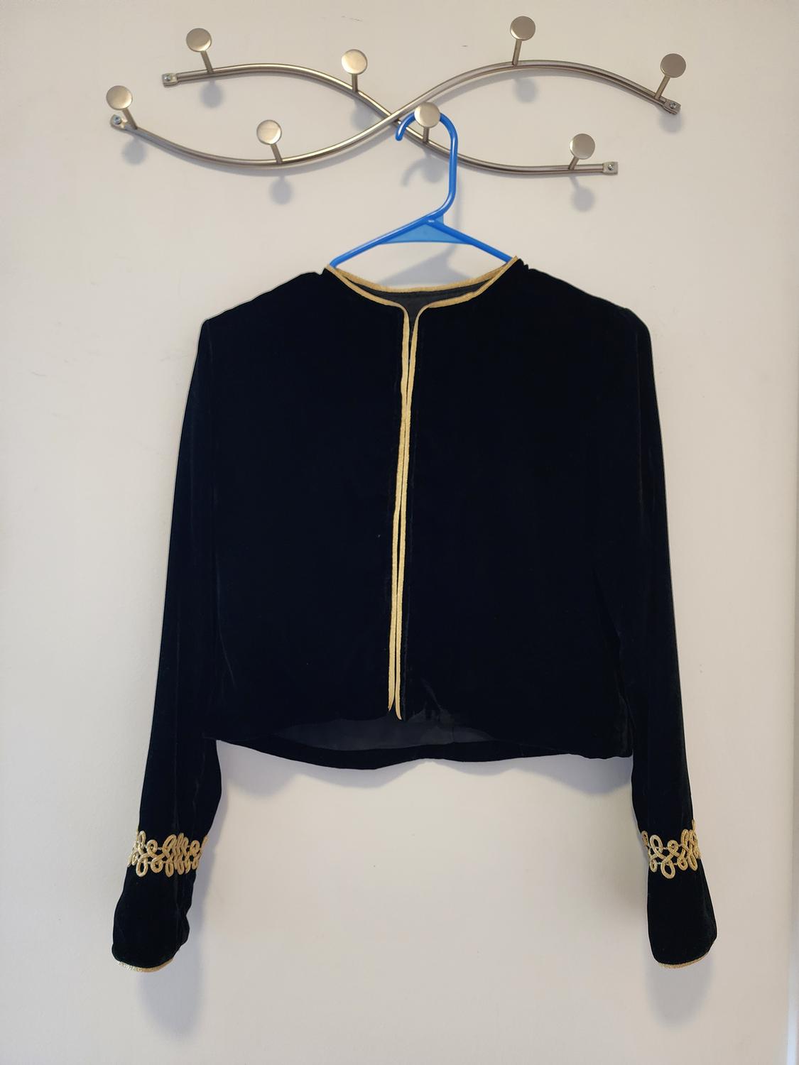 Front view of a black jacket with gold trim and gold embroidery on the cuffs.