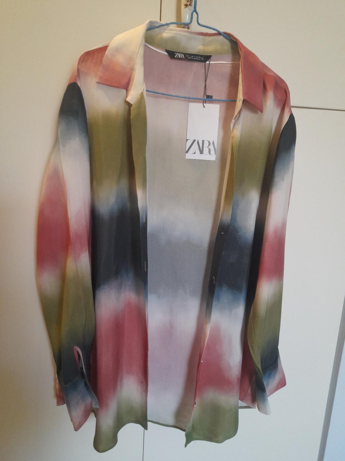 Gradient coloured shirt hanging on a blue hanger. Visible label with the text "ZARA". White wardrobe background.