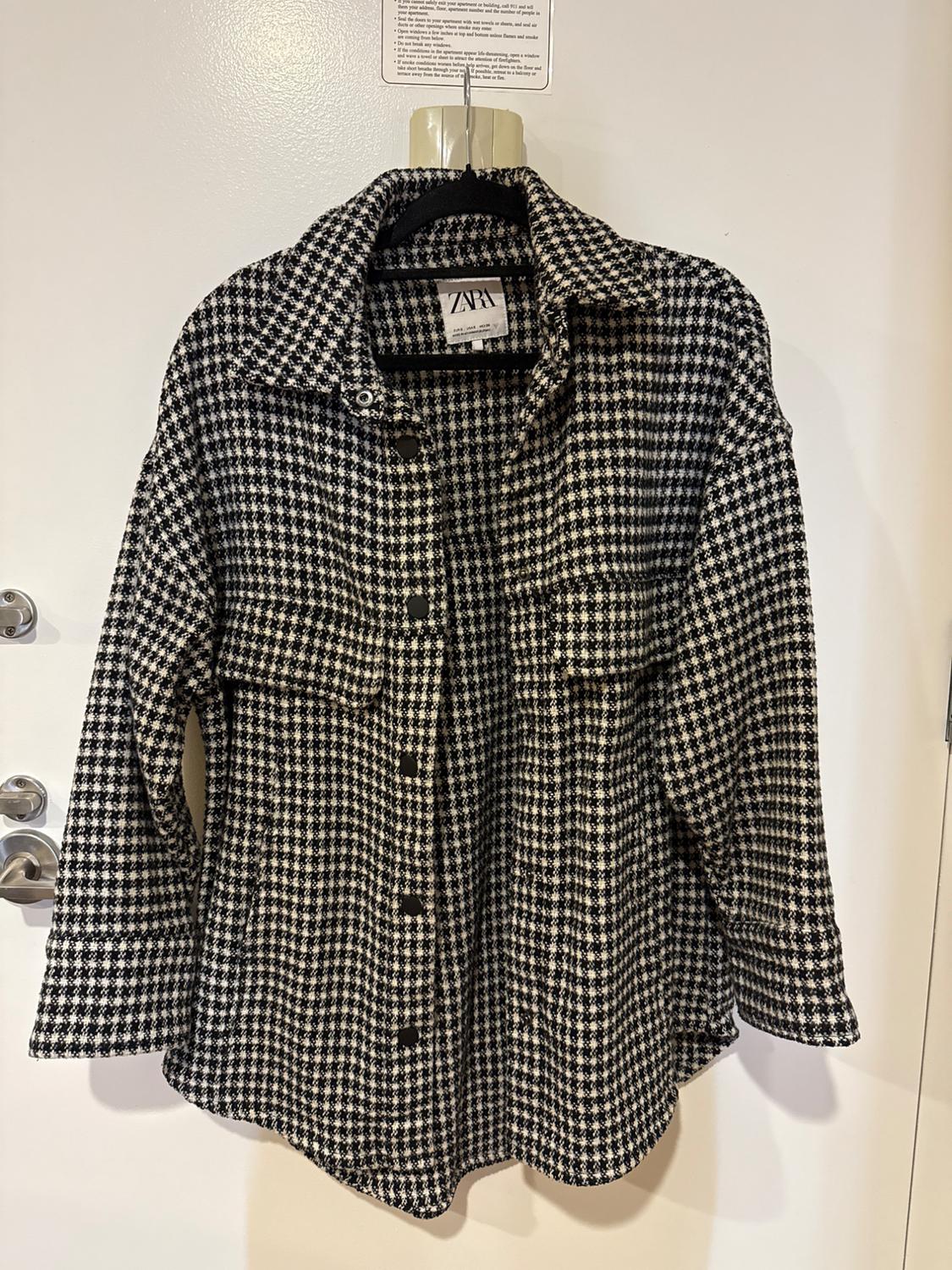 Black and white checked shirt hanging on a hanger. Visible label with the text "ZARA". White background.