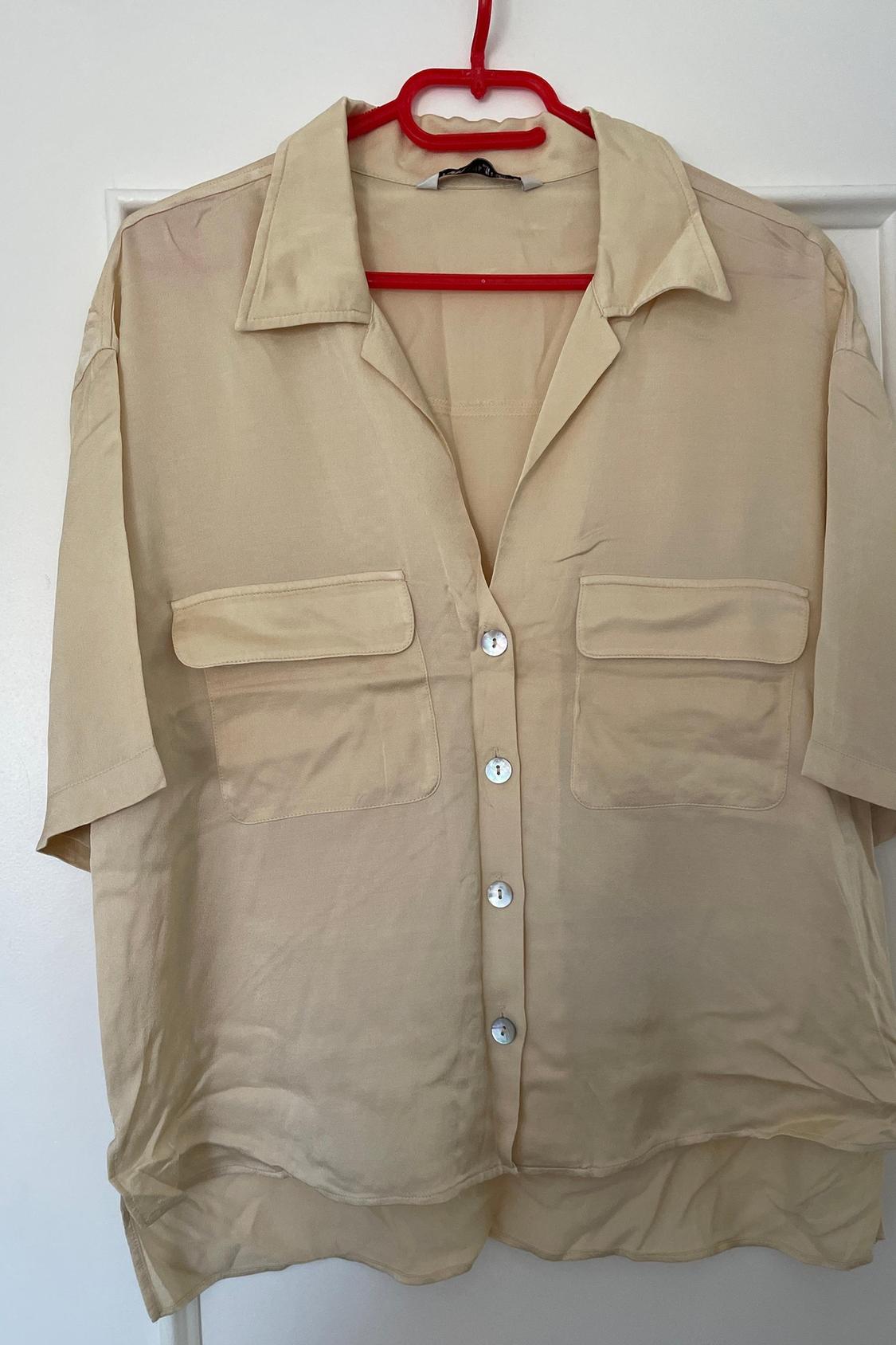 Front view of a beige shirt with front flap pockets and white buttons.