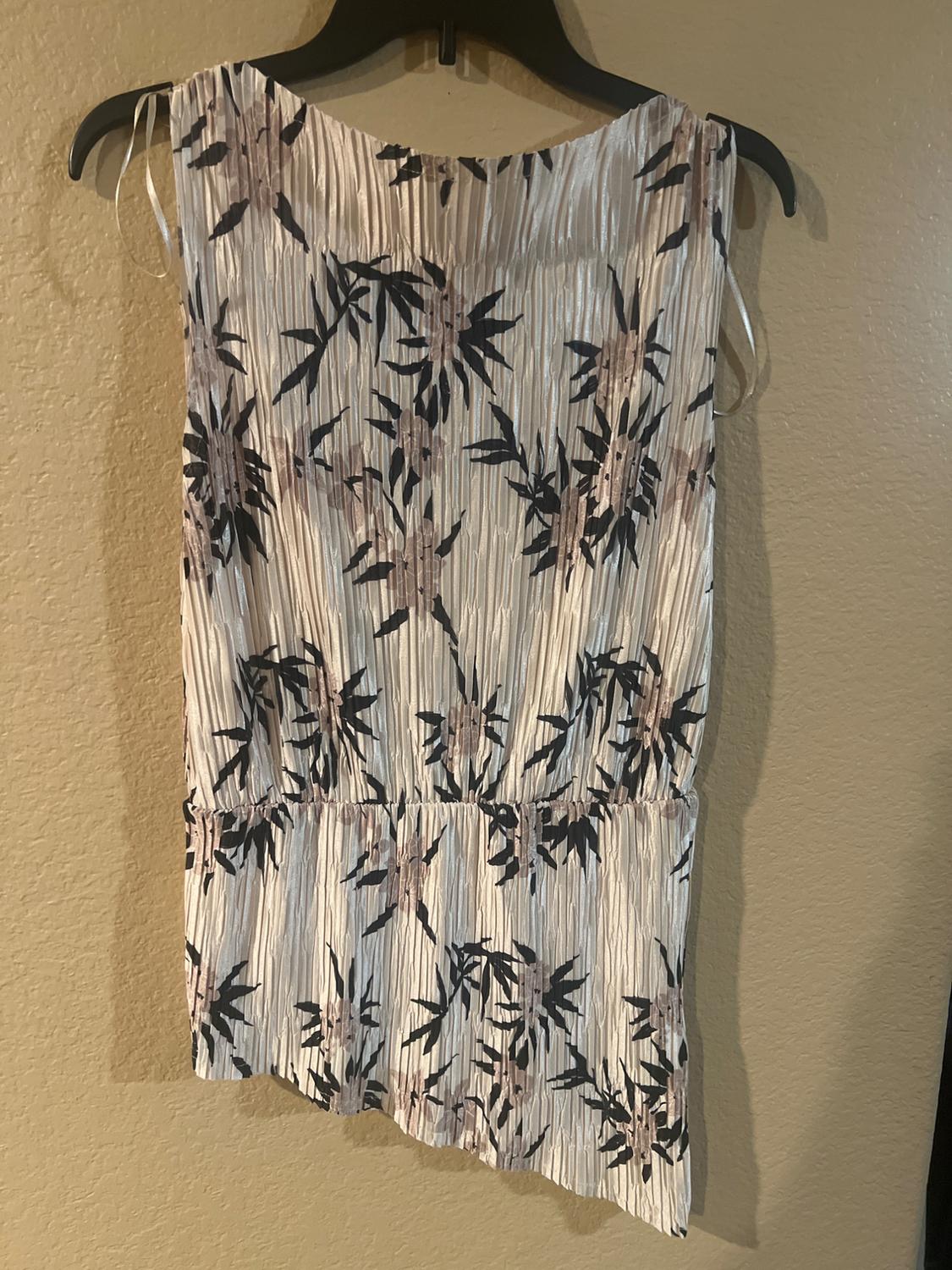 Sleeveless dress with a floral print in dark tones on a light background, hanging on a black hanger against a beige wall.