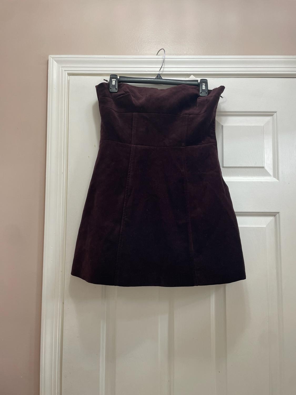 Short strapless dress in dark burgundy hanging on a black hanger over a white door.