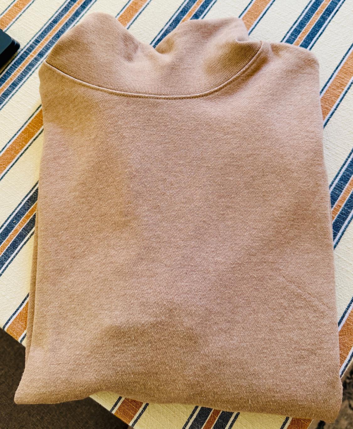 Beige turtleneck sweater folded over a white, blue, and orange striped fabric. Casual and relaxed style composition.