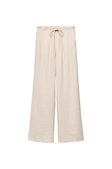 Light beige wide-leg trousers with an elasticated waist and adjustable drawstring. Textured fabric on a white background.