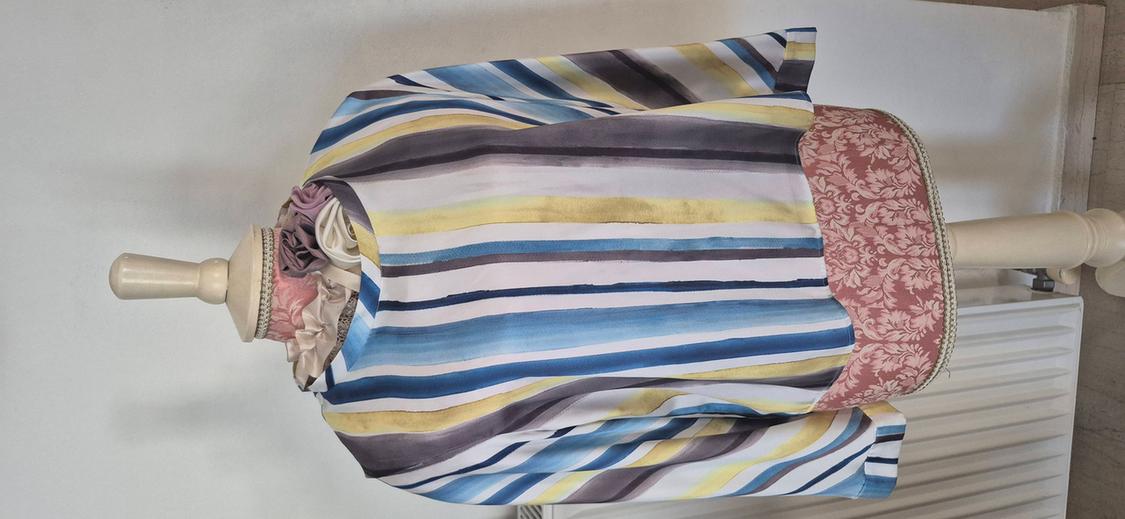 Mannequin with blue, yellow, and purple striped blouse, with pink floral detail on the bottom edge, on a white background.
