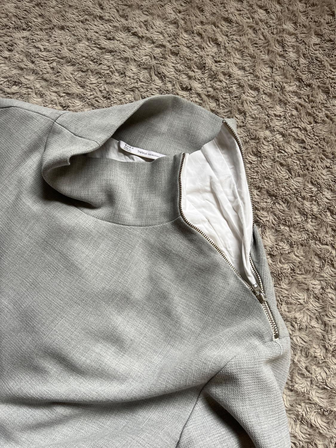 Detail of collar and zipper of gray garment on carpet.