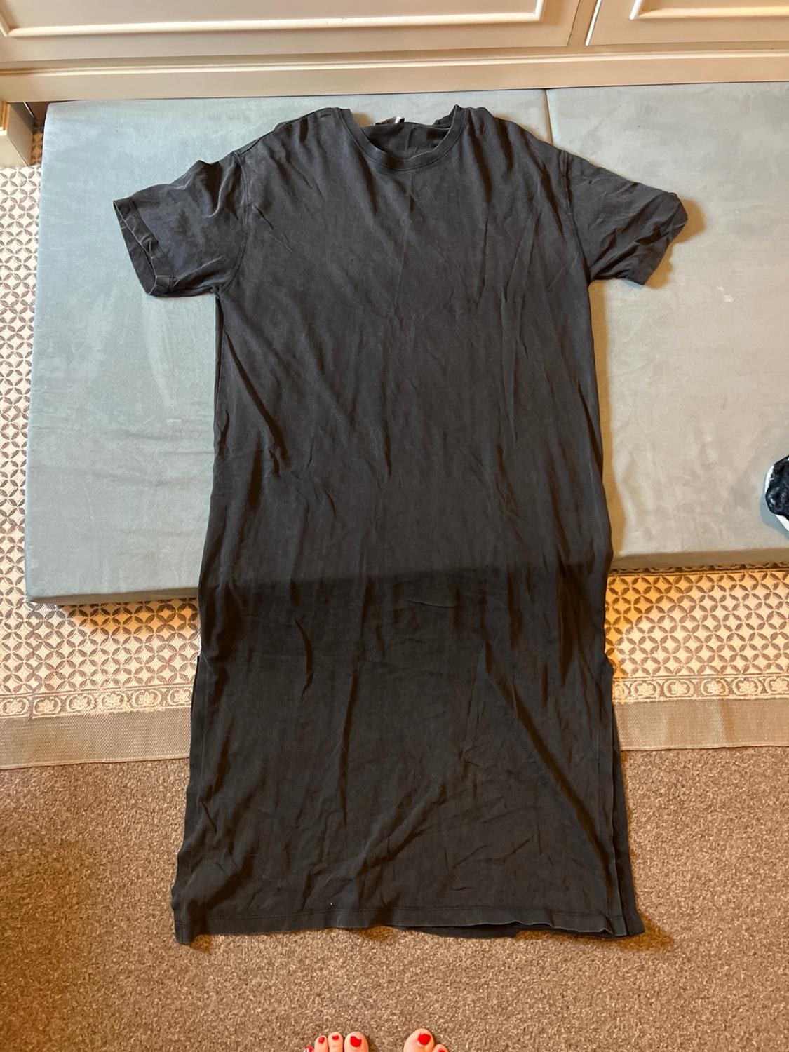 Dark grey short-sleeved maxi dress laid out on a mat and patterned rug. Feet with red toenails can be seen at the bottom.