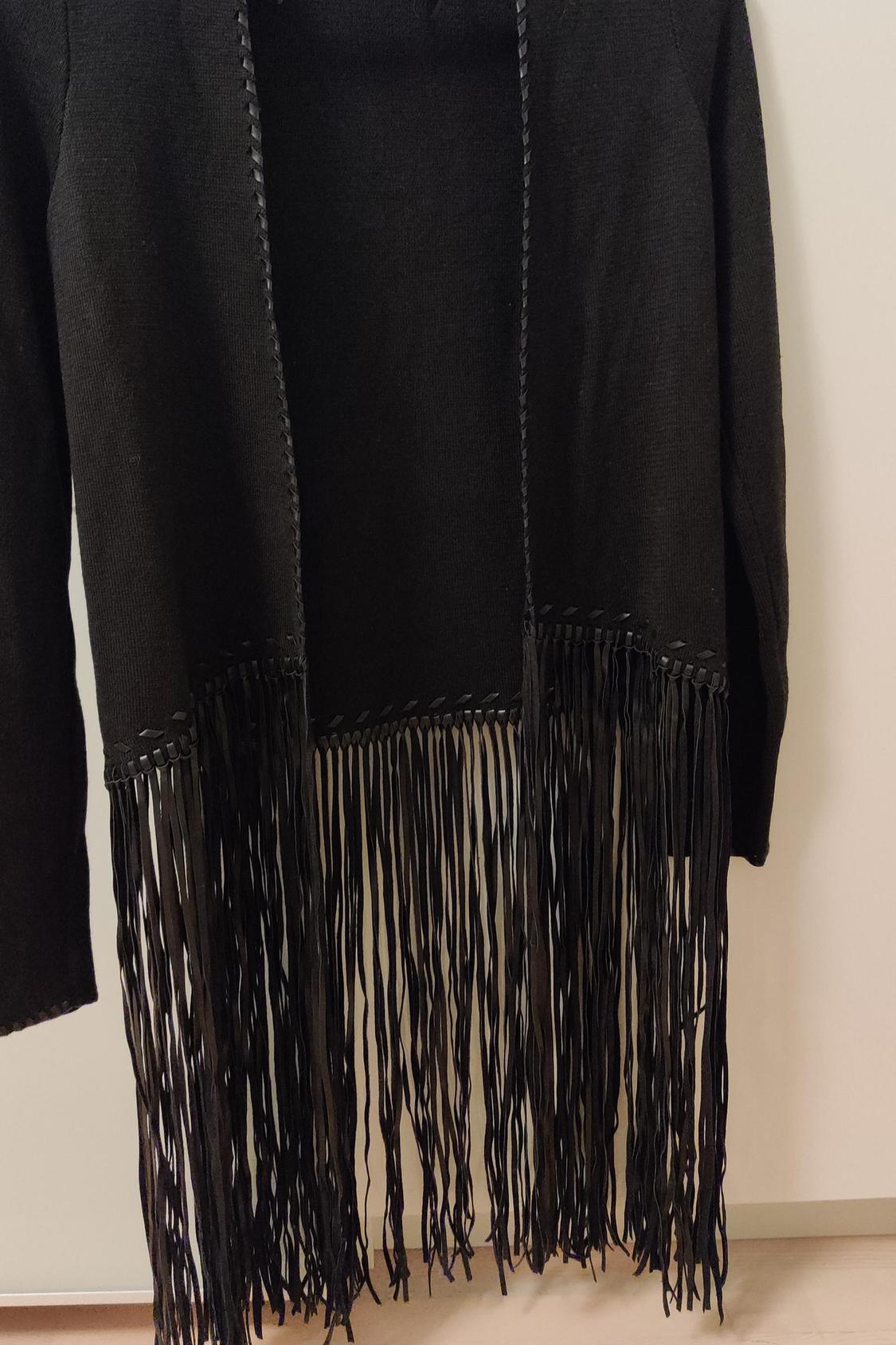 Detail of black cardigan with long fringes on the hem.