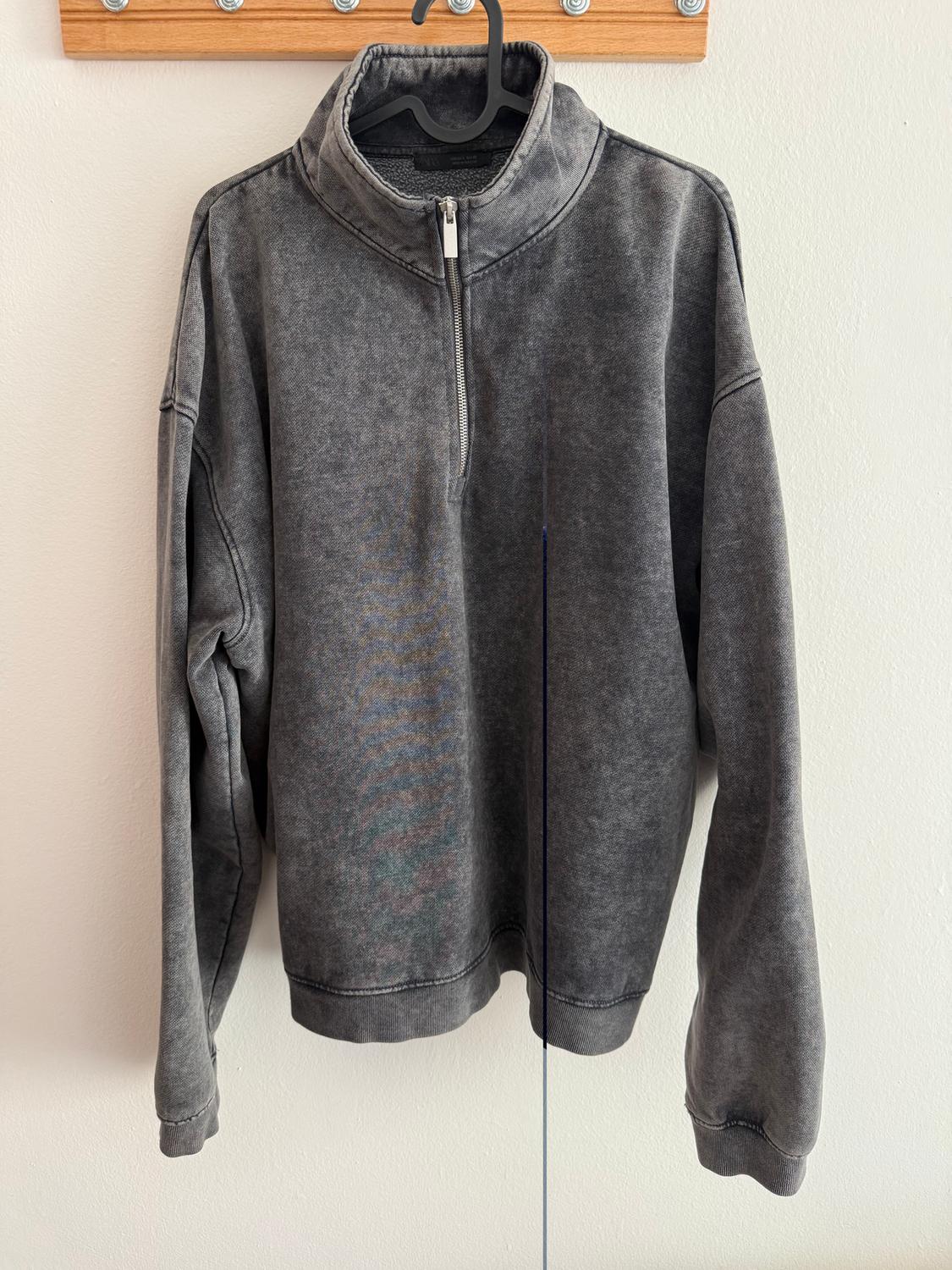 Grey sweatshirt with a quarter-zip, hanging on a black hanger against a white background.