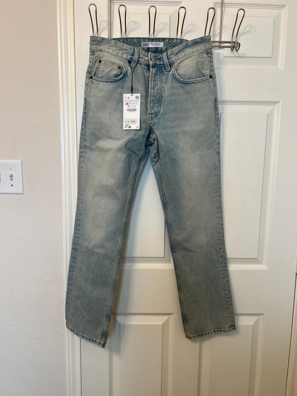 Light blue denim trousers hanging on a white door. They have a label bearing the text 38, and ZARA can be read on the waistband.